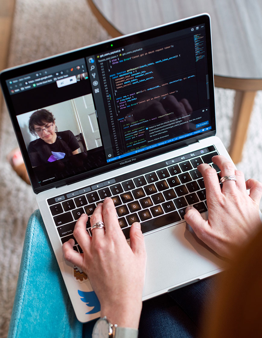 info-10 Laptop mit zwei Händen. Am Bildschirm sieht man einen Videocall und einen Ausschnitt von Code-Schnippsel