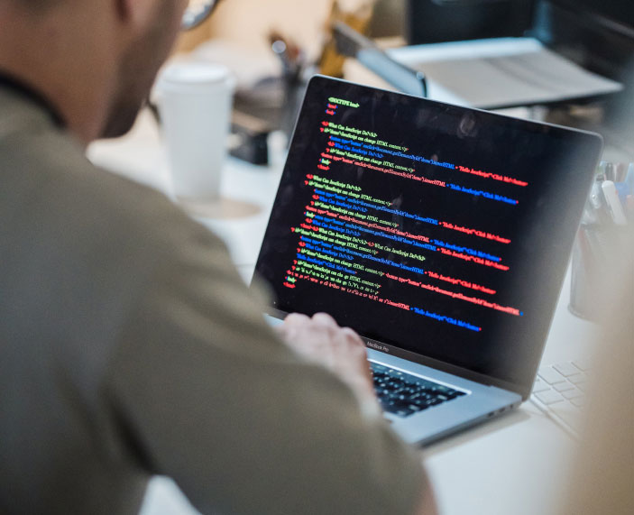 Mann von hinten. Über die Schulter fotografiert und am Laptop ist eine Programmiersprache erkennbar.